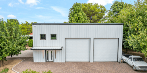 Residential steel buildings featuring a minimalist design with large garage doors and sleek metal siding, set against a green landscape.